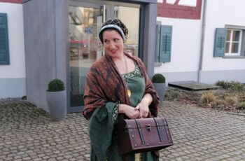 Foto von einer Frau in mittelalterlicher Kleidung mit kleinem Koffer in der Hand vor Fachwekhaus in Singen